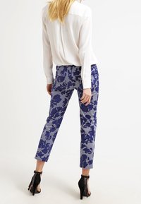 Blå mönstrade byxor med blommiga och geometriska mönster, tillverkade av ett slätt tyg. Matchas med en vit blus och svarta högklackade skor.