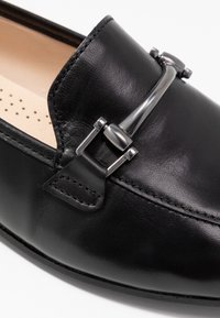 Svarta läderloafers med rund tå, en silverfärgad metallaccent med spänndesign och beige perforerad interiörfoder.