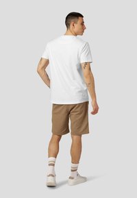 Hvit kortermet t-skjorte med avslappet passform, kombinert med brune shorts. Modellen har på seg hvite sneakers og stripete sokker, som viser en avslappet stil.