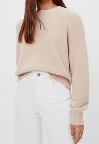 Pull beige pelucheux avec un col rond et des manches longues, assorti à un jean blanc taille haute. Texture douce, coupe décontractée.