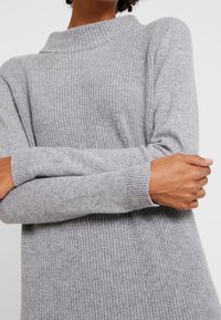 Maglione grigio a maglia con colletto alto, texture a coste e maniche aderenti. Presenta una vestibilità ampia e un materiale morbido per il massimo comfort.