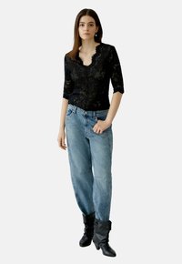 Schwarzes Spitzen-Bodysuit mit gewelltem Ausschnitt und drei Viertelarm, kombiniert mit hellblauen baggy Jeans und schwarzen knielangen Stiefeln.