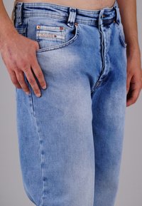 Hellblaue Jeans aus Denim mit einer verblassten Waschung, Kupfernieten und einer Vordertasche mit sichtbaren Stichdetails.