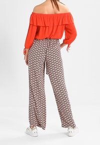 Czerwona bluzka bez ramiączek z falbaniastym dekoltem, zestawiona z szerokimi spodniami w czarno-białym geometrycznym wzorze. Sneakersy z akcentami w kolorze srebra.