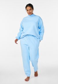 Lichtblauw sweatshirt en joggingbroek set van zachte, gladde stof; het sweatshirt heeft een hoge kraag en de broek een verstelbare trekkoord.
