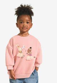 Felpa rosa con vestibilità ampia, caratterizzata da un'illustrazione colorata di animali sul davanti e polsini a coste. Abbinata a pantaloncini di jeans chiari.