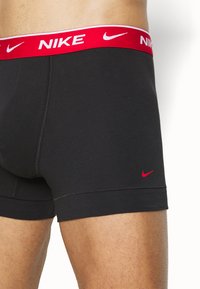 Boxer ajustados de algodón negro con una cinturilla elástica roja que presenta la marca y el logo en blanco de "NIKE". Textura suave con un diseño ceñido.