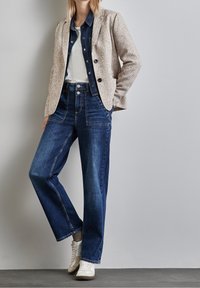 Blazer texturé beige clair sur une chemise en denim noire, associé à un jean bleu taille haute à jambes larges et des baskets blanches.