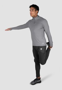 Szary, długi rękaw sportowy top z wysokim kołnierzem, w połączeniu z ciemnoszarymi zwężanymi spodniami z zamkiem błyskawicznym i logo. Model rozciągający się.