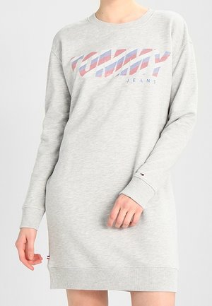 Jasnoszara sukienka z długim rękawem i ściągaczami przy mankietach oraz u dołu, z logo "TOMMY JEANS" w kolorze czerwonym i niebieskim na piersi.