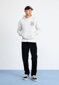 Grijze hoodie met een logo, gecombineerd met zwarte corduroy broek en zwarte sneakers met witte zolen. Eenvoudig ontwerp, relaxte pasvorm, minimale details.