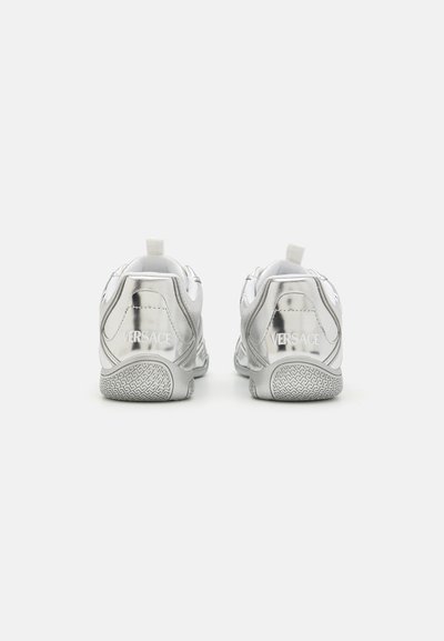 Baskets de sport argentées avec une finition métallique brillante, semelles texturées et une marque bien visible sur le talon. Design léger avec des tirants.