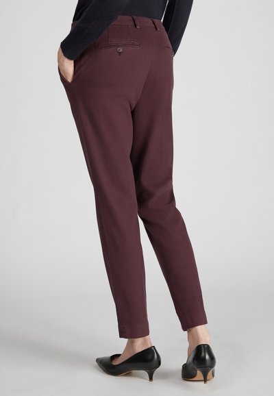 Burgundowe spodnie o slim fit, z tylnymi kieszeniami, akcentami w postaci guzików i gładką fakturą. Noszone z czarnymi szpilkami.