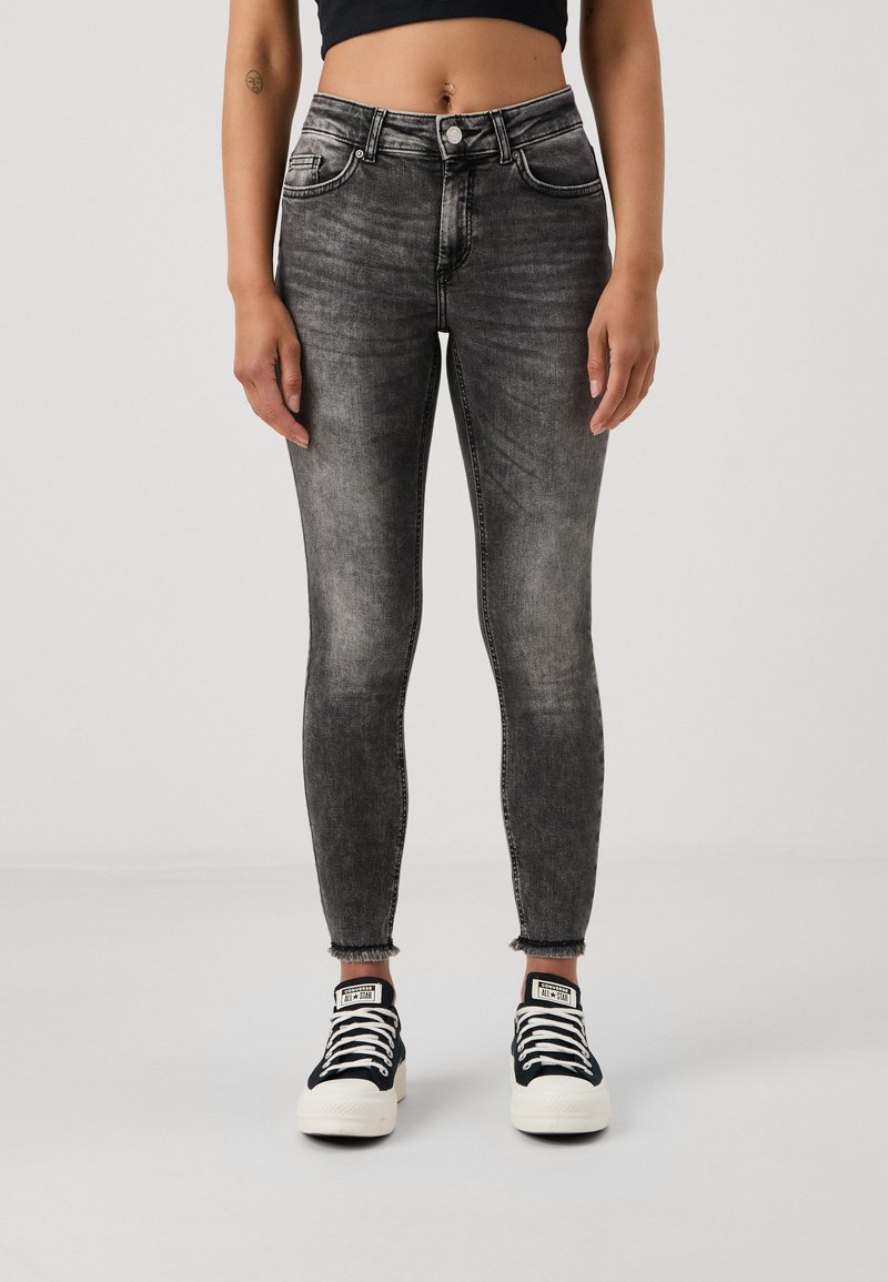 Jeans ajustados en denim negro deslavado, de tiro alto con un ligero desgaste en el dobladillo. Combinados con zapatillas de lona en blanco y negro.