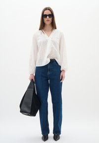 Blusa bianca a maniche lunghe, con texture, abbinata a jeans blu a vita alta. Una borsa nera e tacchi a punta completano il look.