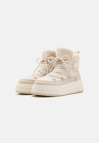 Béžové platformové kotníkové boty s texturovaným, umělým kožešinovým svrškem, plochými šněrovadly a polstrovaným límcem. Obsahují metalické průchodky a robustní pryžovou podrážku.