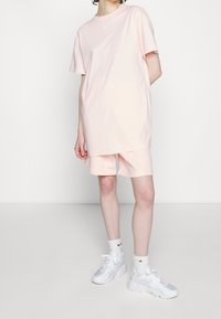 Růžové oversized bavlněné tričko s krátkým rukávem, bílé logo Nike na hrudi, spárované s odpovídajícími růžovými šortkami a bílými sportovními botami.
