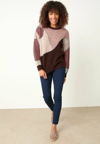 Sweter z wielokolorowymi geometrycznymi wzorami w kolorze bordowym, różowym i kremowym; z akcentami z cekinów. Połączony z granatowymi spodniami slim-fit i beżowymi butami.