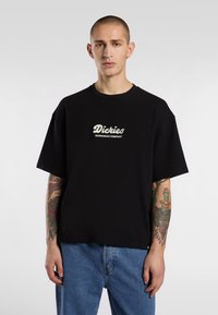 Black cotton t-shirt with a loose fit, short sleeves, and a crew neck; features white embroidered "Dickies Workwear Company" logo on chest.