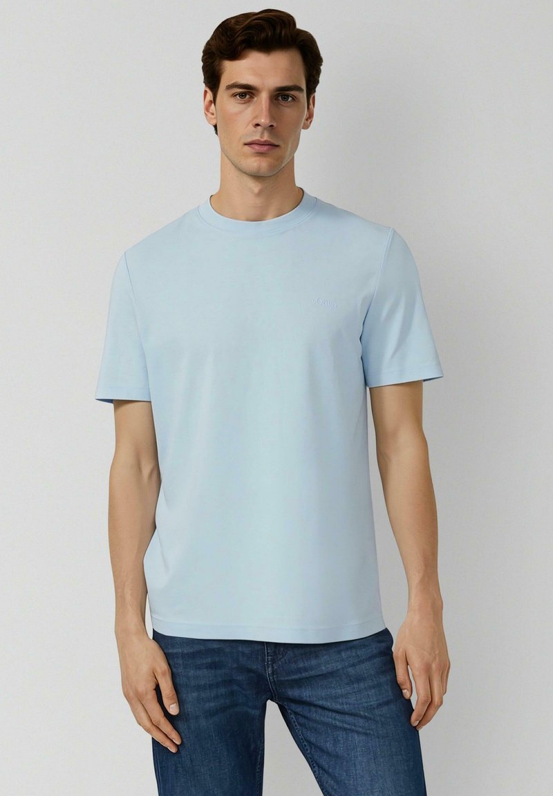 Hellblaues T-Shirt mit kurzen Ärmeln, Rundhalsausschnitt, weicher Textur, mit einem kleinen Logo auf der Brust, kombiniert mit dunkelblauen Jeans.