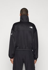 Giacca a pullover nera con colletto alto, polsini e orlo elastici, caratterizzata da dettagli del logo sul retro e sulla manica sinistra. Tessuto liscio.