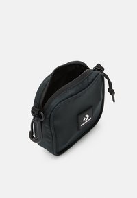 Czarny nylonowy worek zapinany na zamek z teksturowaną powierzchnią, wyraźną naszywką z logo oraz metalowym klipsem z boku do mocowania. Kompaktowy design.