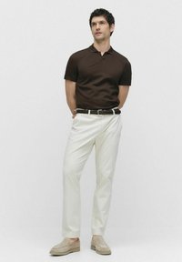 Bruine polo met korte mouwen, witte op maat gemaakte broek en beige suede instapschoenen met een gevlochten donker leren riem. Eenvoudig, strak ontwerp.