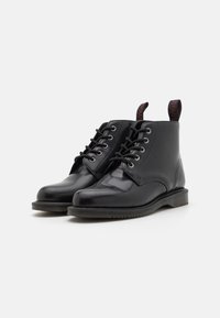 Botas de tobillo de cuero negro con un acabado suave, puntera redonda, diseño con cordones y una lengüeta con logo en el talón. Suela de goma para mayor tracción.