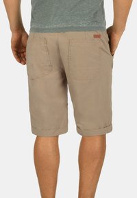 Shorts en coton beige avec des ourlets retroussés, deux poches arrières et une petite étiquette de marque sur la taille. Design léger et décontracté.