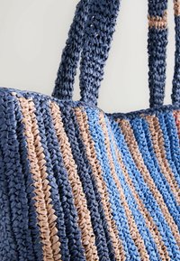 Sac cabas tissé rayé bleu, beige et marine avec de larges anses tressées présenté sur un fond uni.