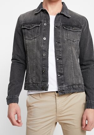 Mørkegrå denimjakke med lange ærmer, knaplukning, brystlommer og klassisk krave. Bæres over en hvid t-shirt.