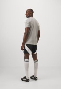 Grå atletisk skjorte med korte ærmer, sorte shorts med hvide diagonale mønstre og sorte fodboldstøvler med hvide detaljer.