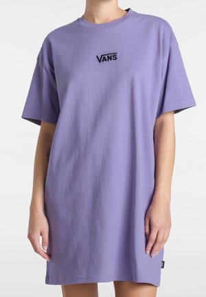 Osoba ubrana w luźną, lawendową sukienkę typu T-shirt marki Vans z krótkimi rękawami i czarnym logo na środku klatki piersiowej.
