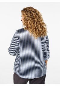 Blouse rayée bleu marine et blanche avec une coupe décontractée, des manches longues et un ourlet arrondi, présentant une texture tissée lisse.