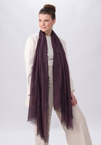Sciarpa intrecciata viola con bordi frangiati, indossata attorno alle spalle di un modello, su uno sfondo neutro.