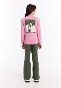 Paarse langemouwtop met een grafische print op de achterkant, gecombineerd met groene skibroeken. De broeken hebben een losse pasvorm en zijn van een zachte textuur.