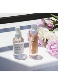 To klare sprayflasker på en hvit overflate: en med en hvit etikett som leser "HERBIVORE ROSE HIBISCUS," den andre med en ferskenfarget etikett for "OUAI ROSE HAIR & BODY OIL."