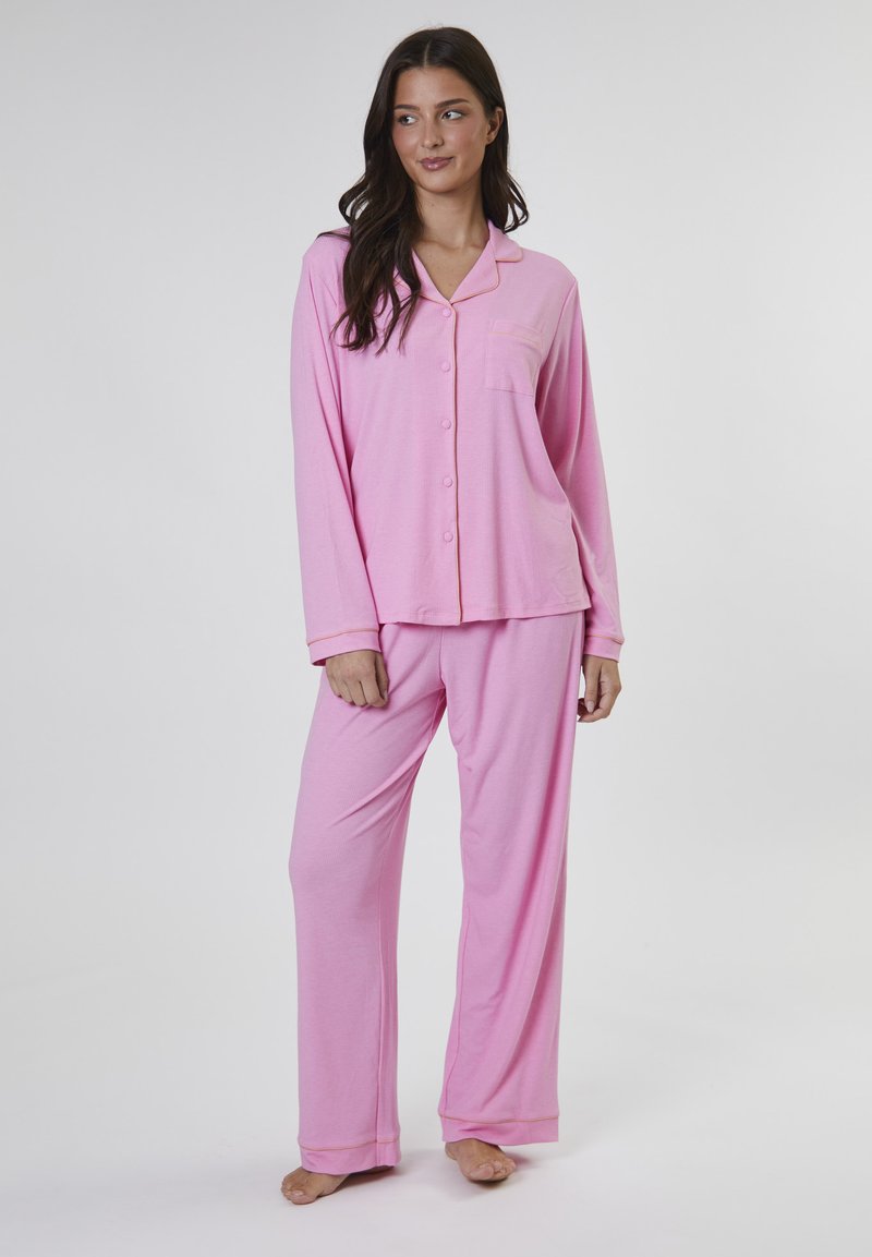 Rosa pyjamaset som inkluderar en långärmad skjorta med knappar och ficka samt matchande löst sittande byxor. Mjuk textur med kontrasterande kant.