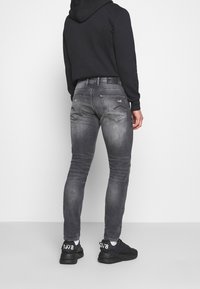 Grijze slim-fit jeans met een vervaagde textuur, twee achterzakken, subtiele stikseldetails, een versleten uitstraling, gecombineerd met zwarte sneakers.