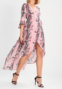 Różowa sukienka w kwiaty, z głębokim dekoltem w kształcie litery V, falbaniastymi rękawami i bocznym rozcięciem. Wykonana z lekkiego materiału z akcentami w tropikalny wzór.