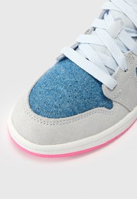 Sneakeril on sinine denimist pealisosa, hall nahkoverlayd ja roosa kummitald. Lõngad on helesinised ja pealisosal on tekstureeritud õmblused.