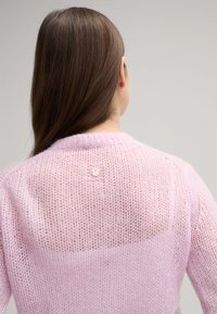 Helles rosa gestricktes Sweatshirt mit einer lockeren, offenen Maschenstruktur; verfügt über einen runden Ausschnitt und einen kleinen dekorativen Knopf auf der Rückseite.