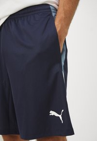 Calções atléticos azul-marinho feitos de um tecido leve, com um cós elástico, uma faixa lateral em azul claro e um logótipo da Puma em branco.