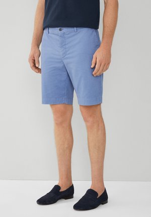 Lysblå bomuldsbukser med knaplukning foran og sidelommer. Bæres med marineblå ruskindsloafers. Glat tekstur, knælængde design.