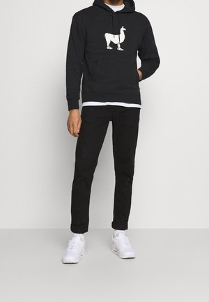 Sudadera negra con un gráfico de llama blanca en el pecho, combinada con pantalones negros ajustados y zapatillas blancas, que incluye un bolsillo frontal y capucha con cordón.