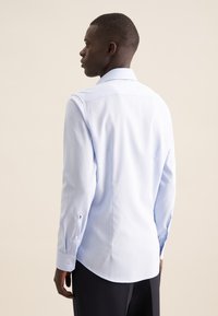 Camicia azzurro chiaro a maniche lunghe con colletto classico, polsini abbottonati e orlo curvo, realizzata in tessuto liscio e strutturato.