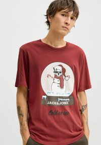 Rode T-shirt met korte mouwen, versierd met een festieve sneeuwmanafbeelding met een schedelontwerp, die een sjaal en hoed draagt, en de tekst "Koud als ijs" eronder.