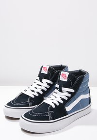 Høje sneakers i mørk navy og lyseblå ruskind. Har hvide snørebånd, fremtrædende syninger og et hvidt bølge-logo på siden.