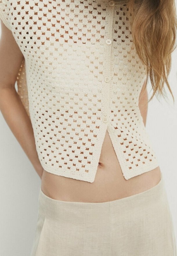 Helles beige, cropped Top mit einem offenen Strickmuster, ausgestattet mit einer Knopfleiste und einem gespaltenen Saumdesign. Strukturiertes Garn sorgt für visuelles Interesse.