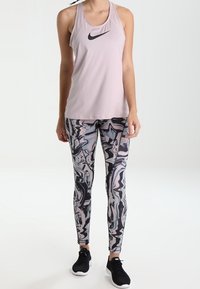 Top atlético sin mangas de color rosa claro con el logo negro de Nike, combinado con leggings ajustados que presentan un patrón en espiral de color negro, rosa y gris.